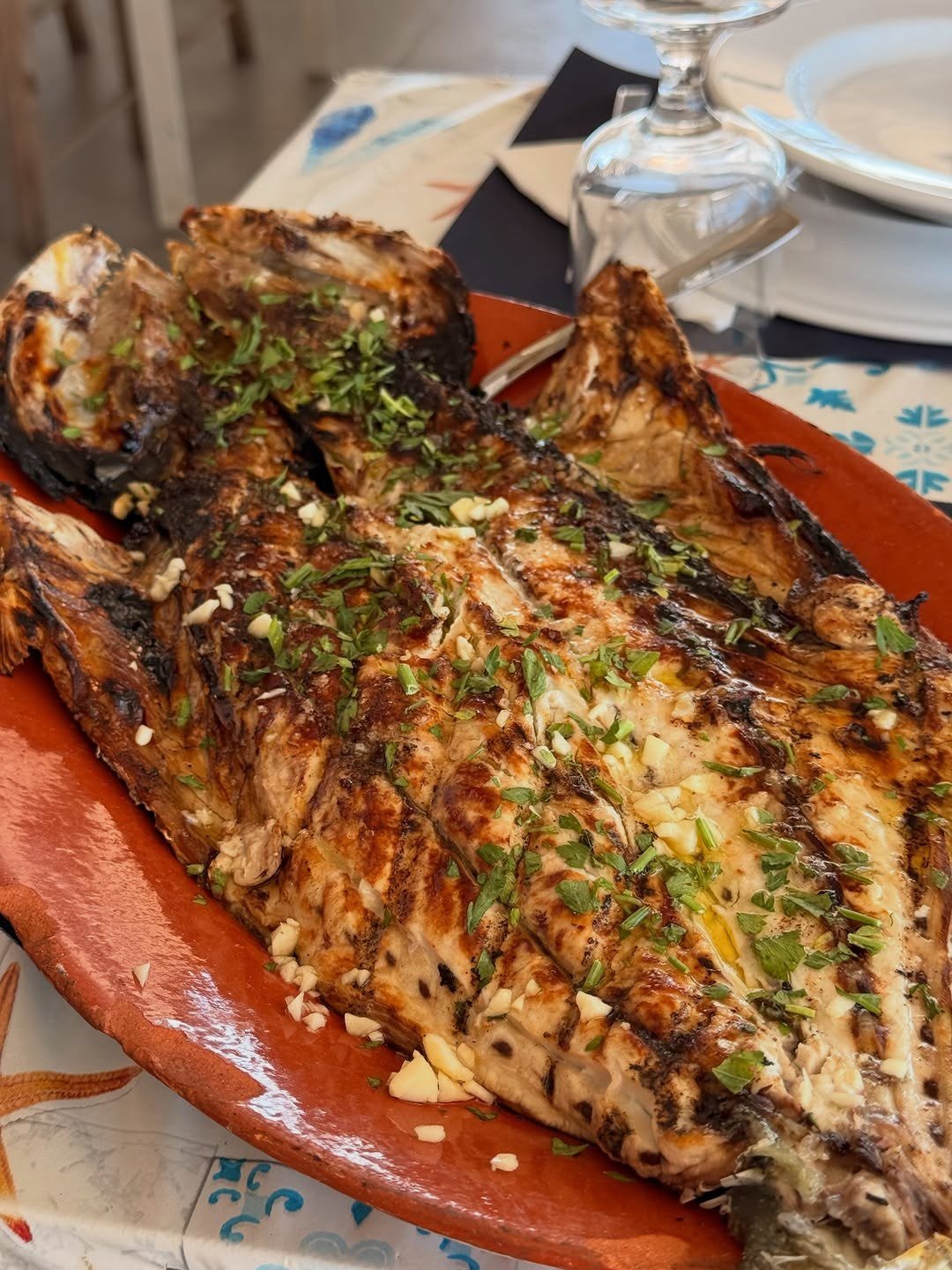 Peixe grelhado inteiro num prato de barro, com alho e salsa picados por cima